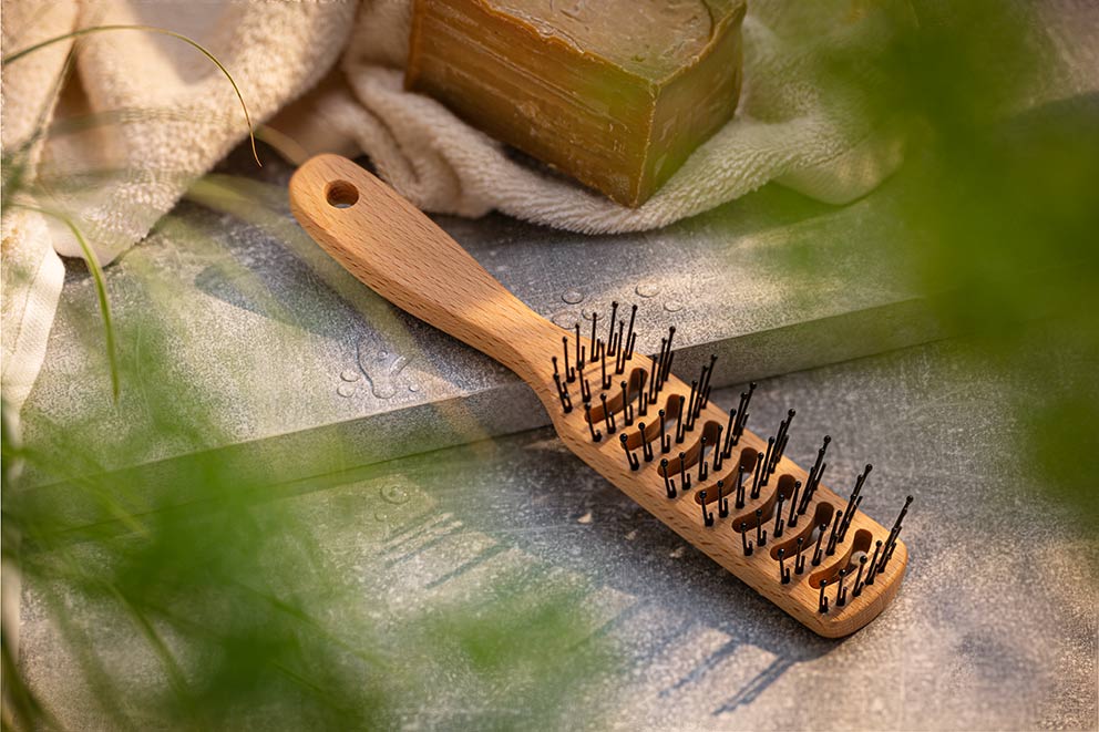 Eine Haarbürste aus Holz liegt neben einer Seife.